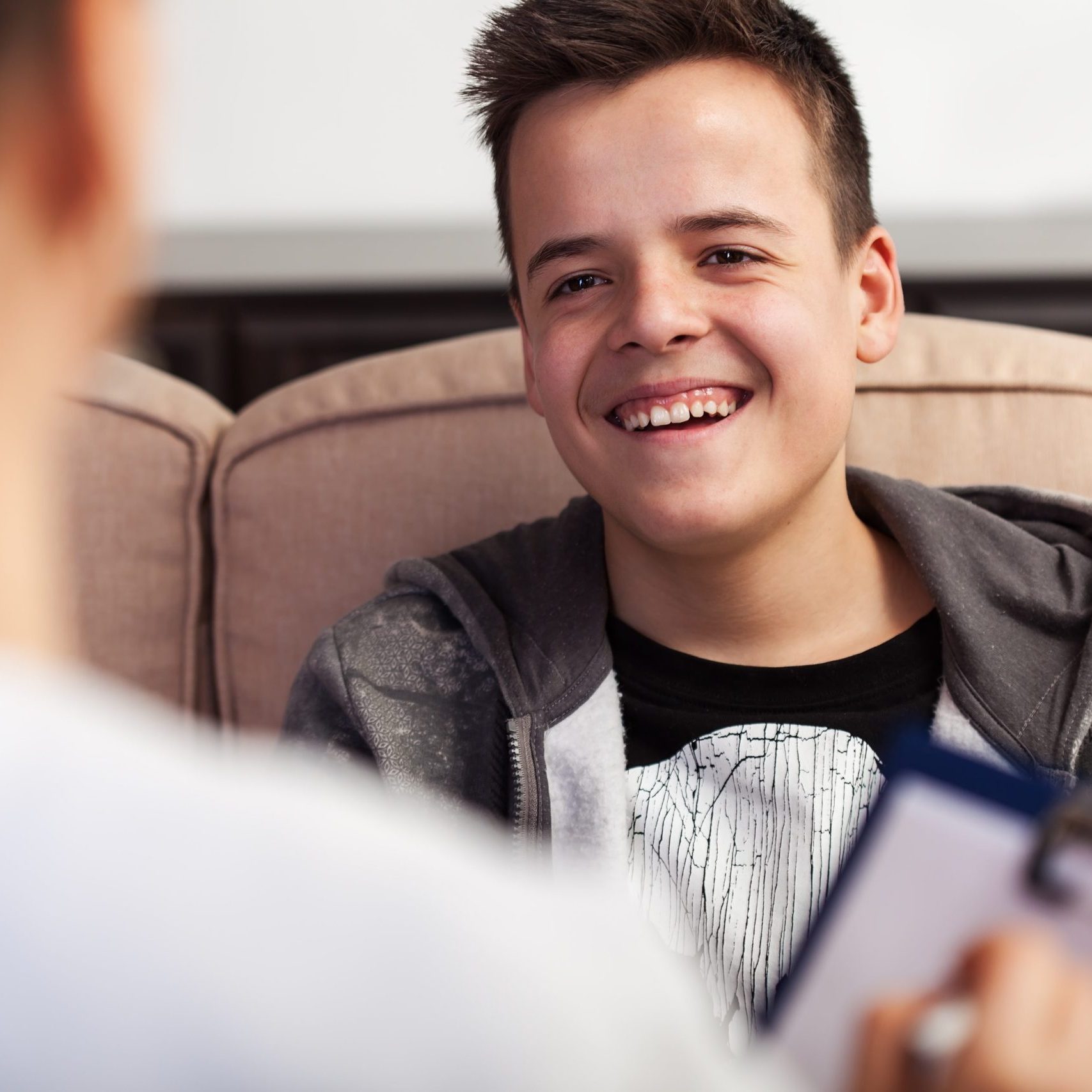 Young teenager boy laughing at counseling professional in foreground, not taking it seriously, deny and underrate the importance - close up